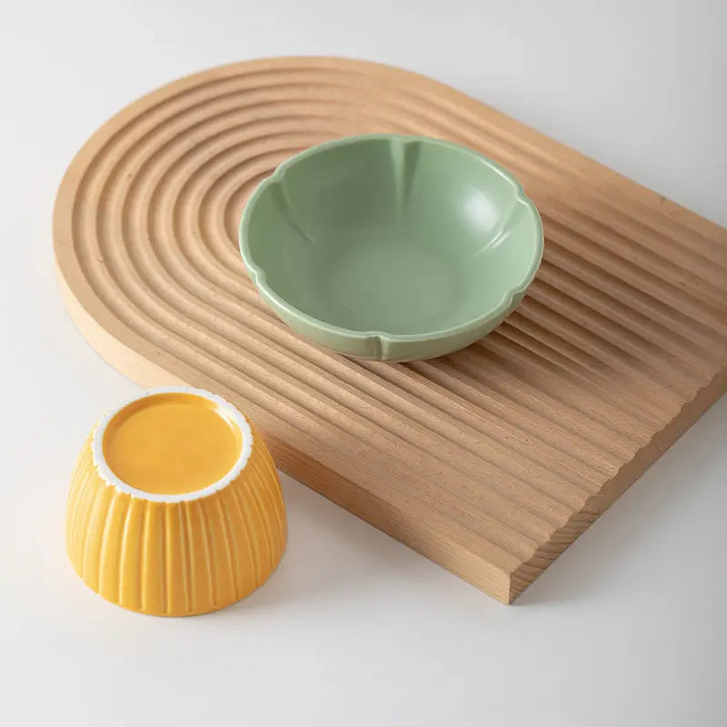 Ceramic feeding bowls in candy colors for cats, featuring pink and green options on a decorative board.