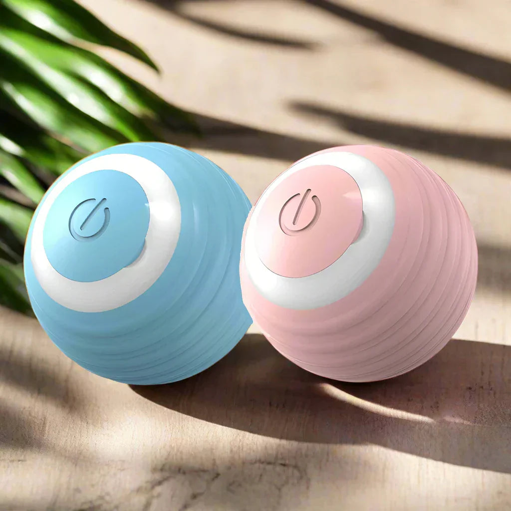 Two ZoomieRoller™ Smart Toy balls in blue and pink on a wooden surface with greenery in the background.